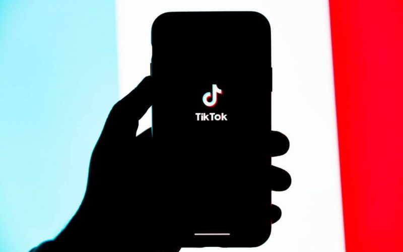 Silhouette of hand holding an iPhone displaying the TikTok logo
