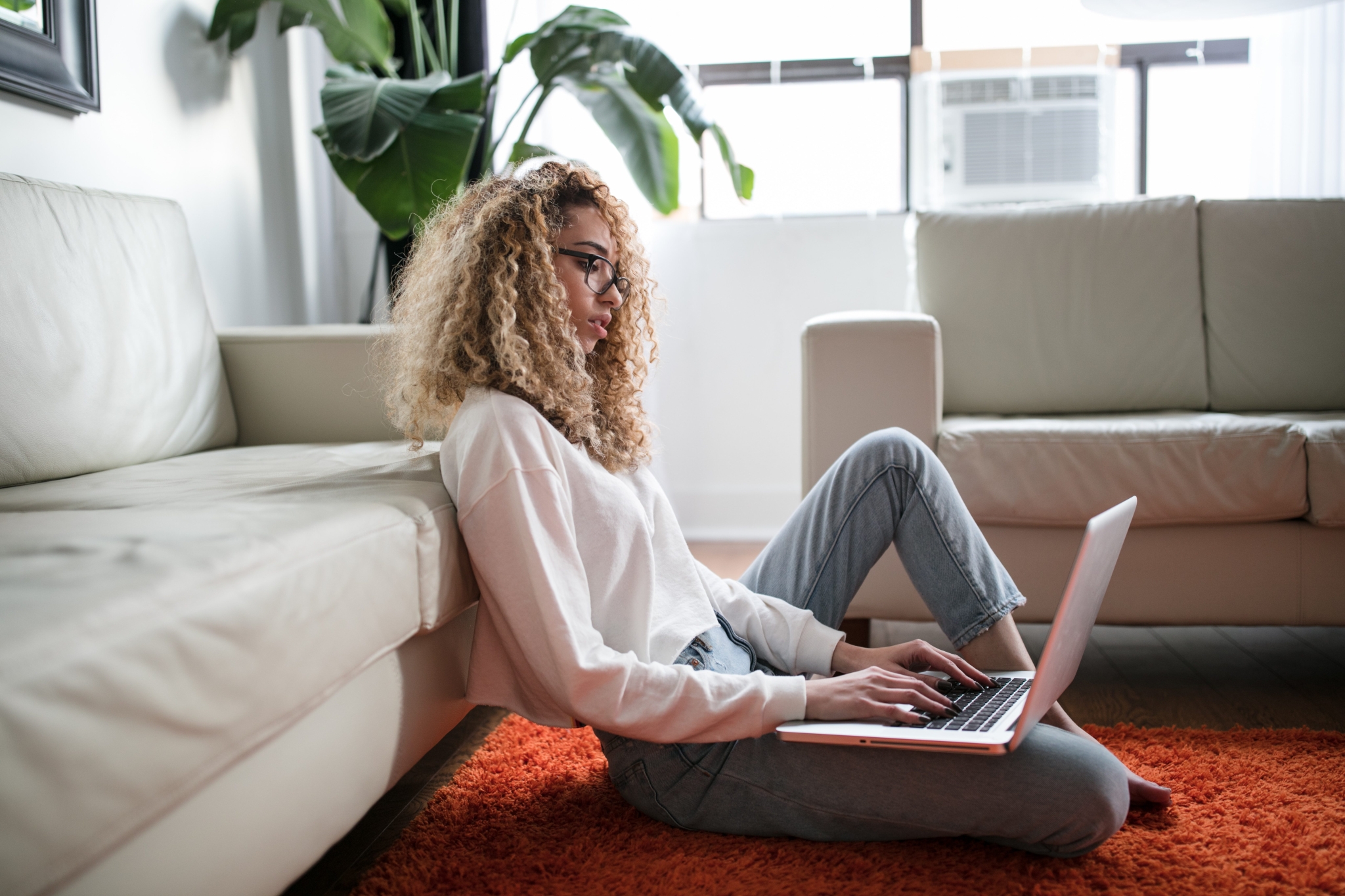 Woman sat on an orange rug whilst on her laptop